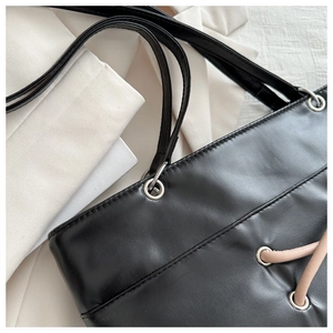 Close-up of black leather tote bag with beige rope detail and silver eyelets on the top