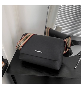 Détail du sac bandoulière en cuir noir avec sangle rayée et garniture argentée
