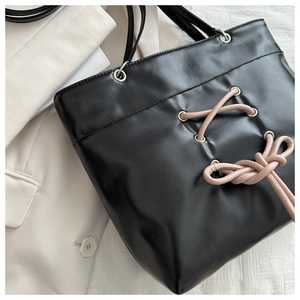 Detail of black leather tote bag featuring a pink bow tie and soft leather texture