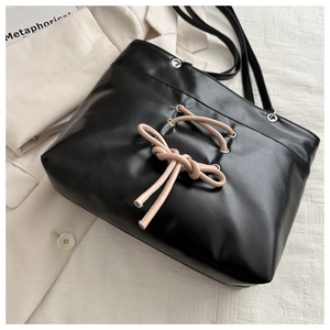 Detail of black leather tote bag featuring pink lace-up bow design and silver eyelets