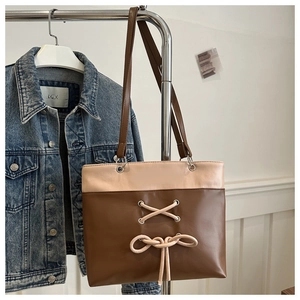 Close-up of two-tone brown tote bag with bow drawstring detailing and matte leather texture