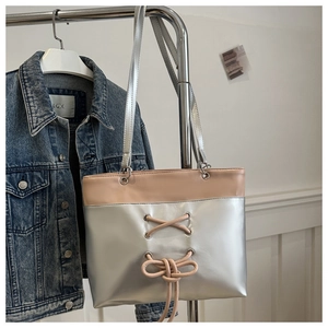 Detail of silver and beige tote bag with crossover ribbon and bow on denim jacket