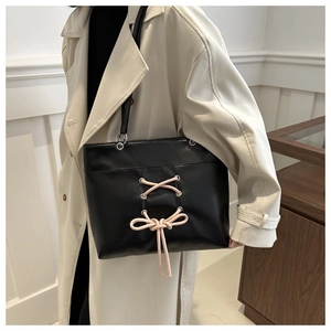 Detail of black faux leather tote bag with pink lace-up bow and silver metal hardware