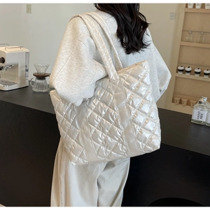 Close-up of quilted glossy white tote bag with wide shoulder straps in a cafe setting
