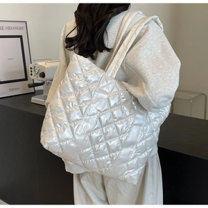 Quilted glossy pearl white tote bag on model shoulder in a cozy cafe setting
