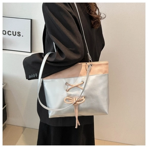 Detail of silver metallic PU tote bag with pink stitching and decorative bow on model