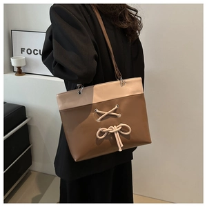 Detailed macro view of the two-tone tote bag featuring beige bow and brown leather texture
