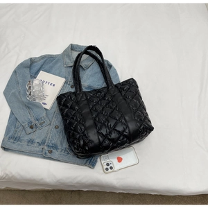 Macro view of black quilted glossy fabric and diamond stitching on shoulder tote bag