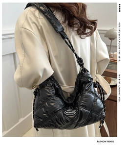 Detail of black quilted puffer bag showing woven rope strap and fashion logo on model