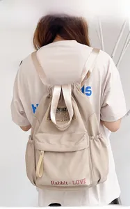 Détail du sac à dos beige en nylon avec cordon, poche zippée avant et textures de sangle