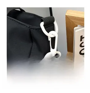 Dettaglio del gancio in plastica bianca e della tracolla intrecciata su borsa in nylon nero