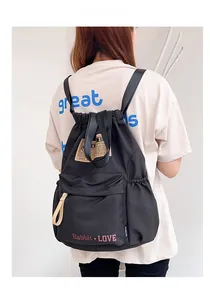 Détail d'un sac à dos en nylon noir avec cordon de serrage, logo rouge et poche latérale