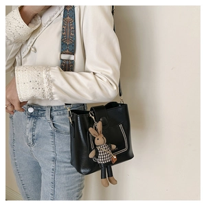 Detail of black leather bucket bag with boho strap and cute rabbit charm on a model