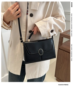 Detail of black crossbody envelope bag featuring golden oval clasp and adjustable strap