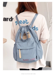 Détail du sac à dos bleu clair en nylon avec cordon, étiquette vintage et poche avant