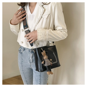 Detail of black leather bucket bag with retro patterned strap and rabbit plush pendant