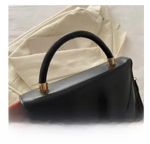 Detail of black leather handbag featuring round gold buckle and sturdy top handle
