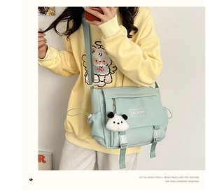 Détail du sac messager en toile vert menthe avec un porte-clés panda en peluche