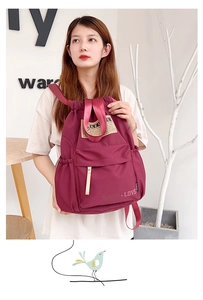 Détail du sac à dos en nylon bordeaux montrant l'écusson du logo et la poche zippée avant