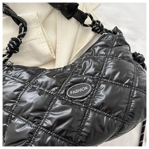 Detail of quilted glossy black shoulder bag with woven rope handle and fashion label