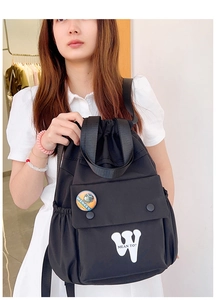Dettaglio dello zaino nero in nylon con coulisse, distintivo a scimmia e tasca laterale scuola