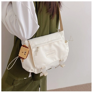 Détail du sac messager en nylon blanc avec boucle latérale et breloque en peluche biscuit
