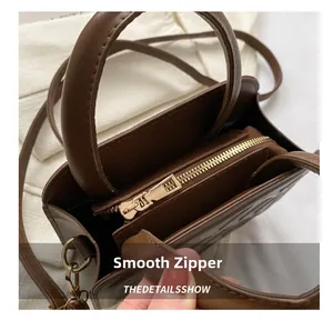 Detail view of smooth metal zipper and top handle on brown quilted leather crossbody bag