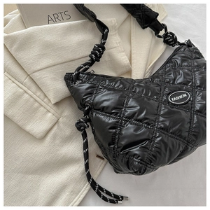 Detail of black quilted shoulder bag featuring glossy finish and woven strap textures