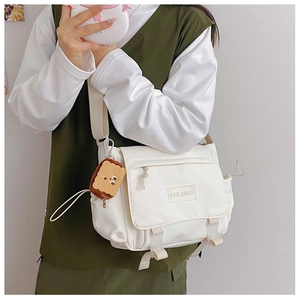Détail du sac messager en toile blanche avec boucles et breloque en peluche biscuit