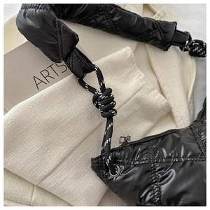 Detail view of black quilted down crossbody bag with puffy texture and knot strap