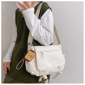 Détail du sac messager en toile blanche avec boucles et breloque biscuit mignonne