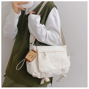 Gros plan sur un sac messager en nylon blanc avec charm en peluche biscuit et bandoulière