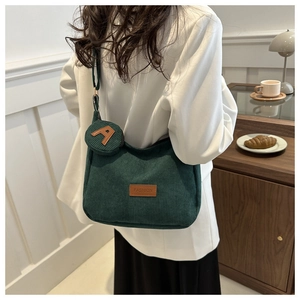 Detail of dark green corduroy shoulder bag with leather label and mini round pouch charm
