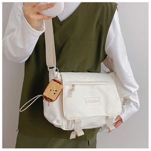 Détail du sac messager en nylon crème avec étiquette DAILAISHI et porte-clé biscuit