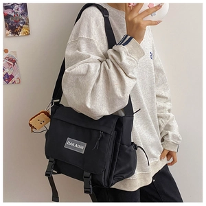 Détail de la besace en nylon noir avec rabat, doubles boucles et plaque de logo