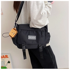Détail de la besace noire en nylon avec boucles et pendentif en peluche biscuit