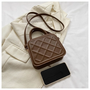 Close-up of small dark brown quilted crossbody bag with gold hardware and phone for scale