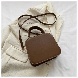 Detail view of brown quilted crossbody bag with top handle on minimalist outfit background