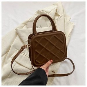 Detail of dark brown quilted crossbody bag with top handle on white blazer