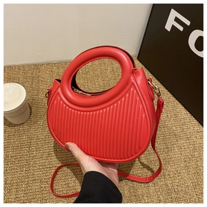 Detail einer roten halbmondförmigen Handtasche mit vertikaler Streifenprägung und Goldreißverschluss