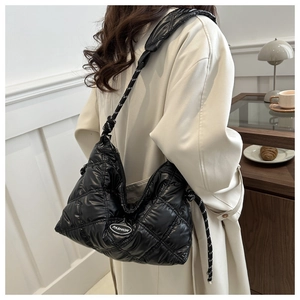 Detail of black quilted puffer bag with Fashion logo and woven strap worn by model