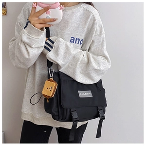 Détail du sac messager en nylon noir avec boucle et charmant pendentif en forme de biscuit