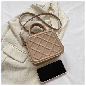 Macro shot of a beige quilted PU leather crossbody bag next to a smartphone for scale
