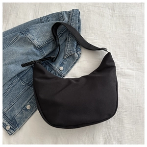 Detail of minimalist black nylon crescent bag with adjustable strap on denim jacket