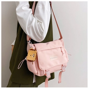 Détail du sac bandoulière en nylon rose avec boucles à rabat et pendentif biscuit en peluche