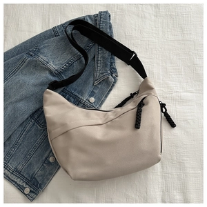 Detail of a beige crescent crossbody bag with zipper and black woven cord puller