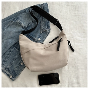 Close-up of beige moon bag with black adjustable strap and woven zipper pull detail