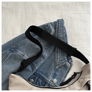Detail view of beige canvas dumpling bag with black adjustable strap and cord zipper pull