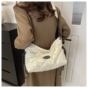 Detail of cream quilted down bag with braided rope strap and tassels on model shoulder