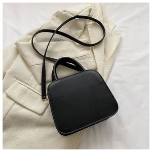 Close-up of matte black quilted square handbag with handles and a long shoulder strap